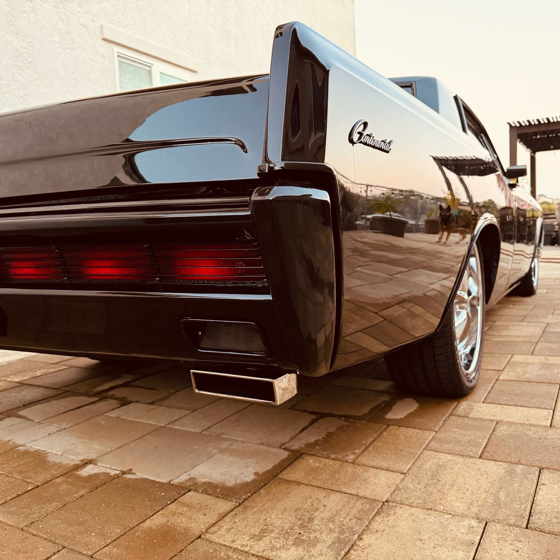 Black classic car parked on a brick driveway, rear three-quarter view, with chrome details and tinted taillights.