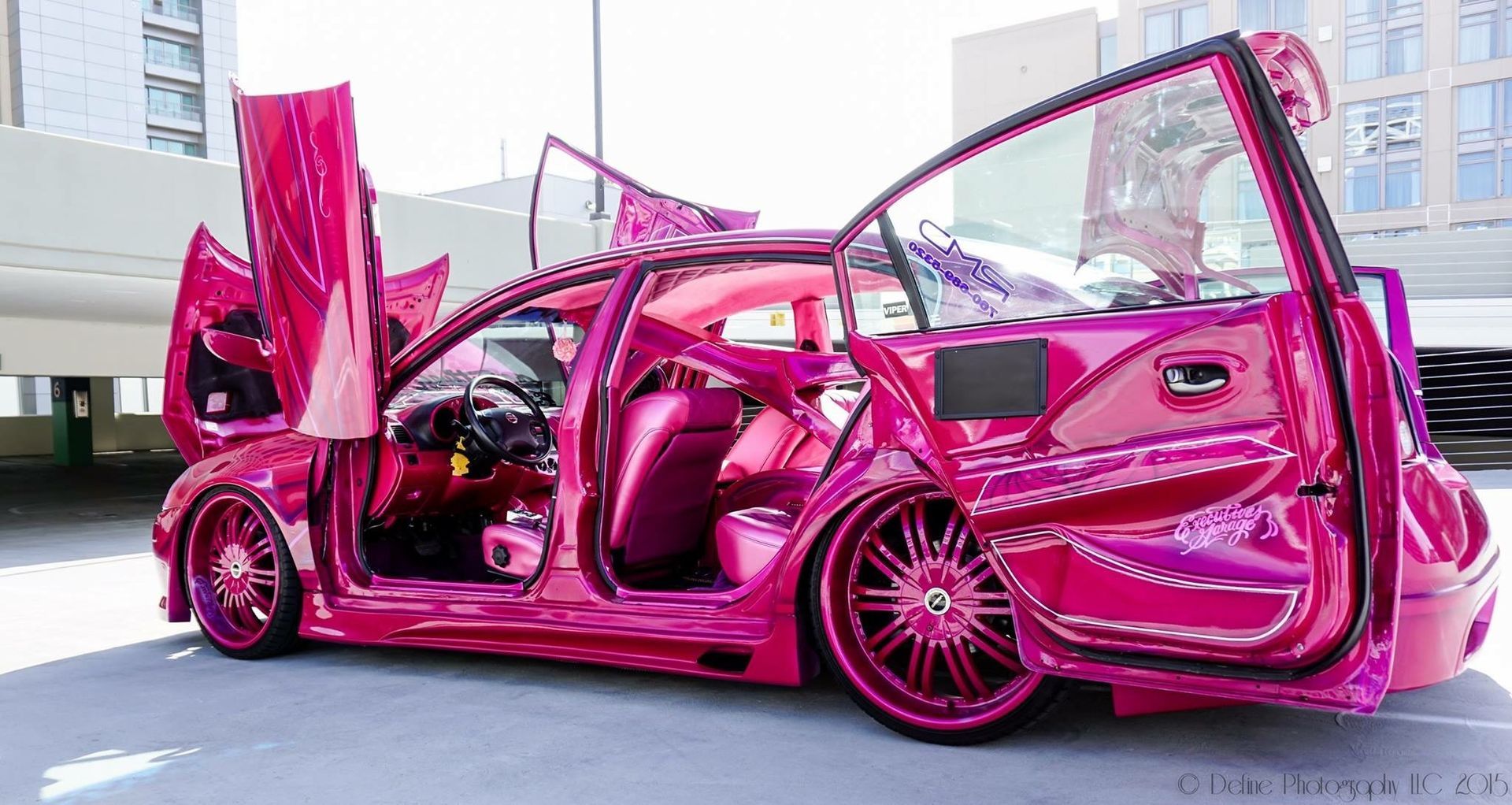 Hot pink custom sports car with doors open, displayed indoors under bright lights.