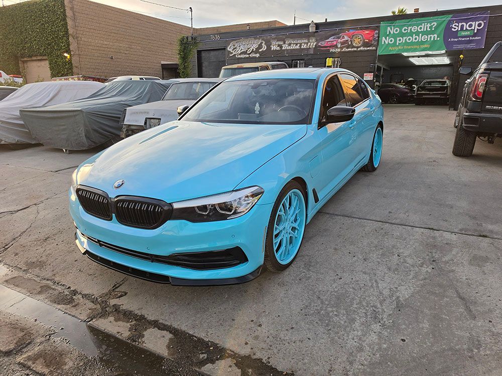 Bright blue BMW parked in a lot, front view, with covered cars and signage in the background