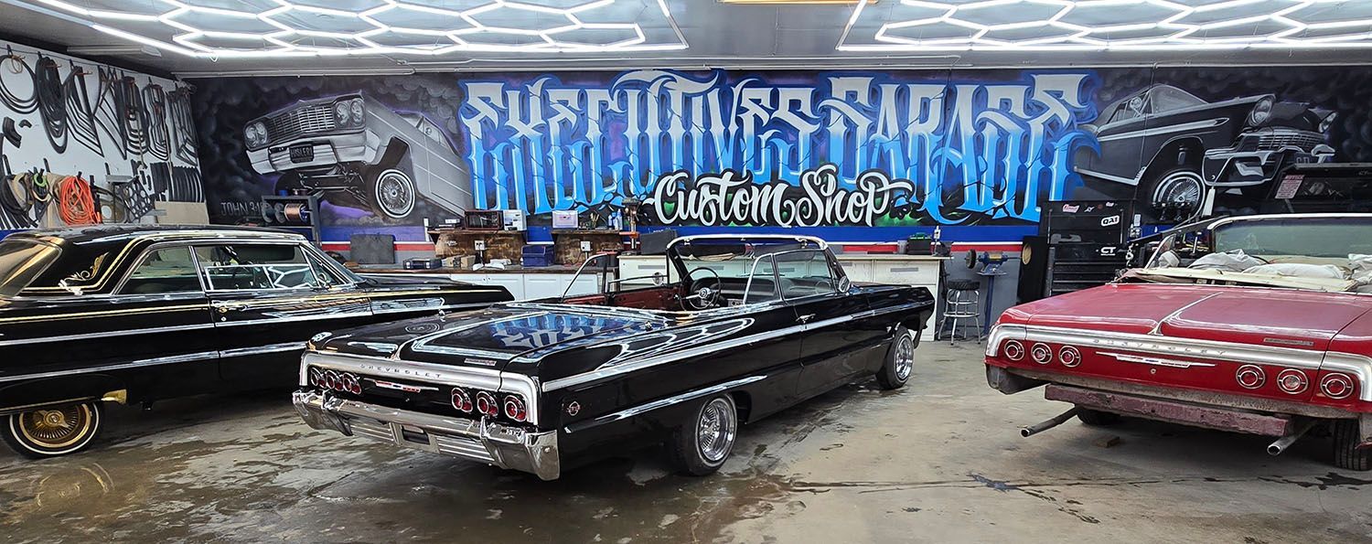 Classic lowrider cars parked before a mural reading “Nefarious Rituals” on a street wall.
