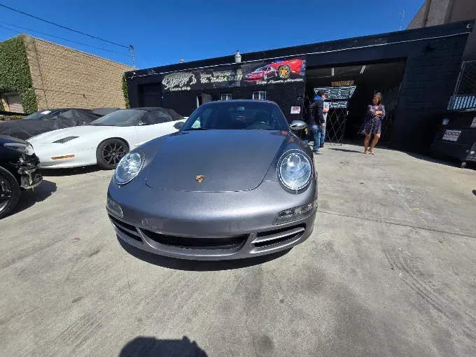 Gray Porsche parked outside a shop, with people standing nearby on a sunny day