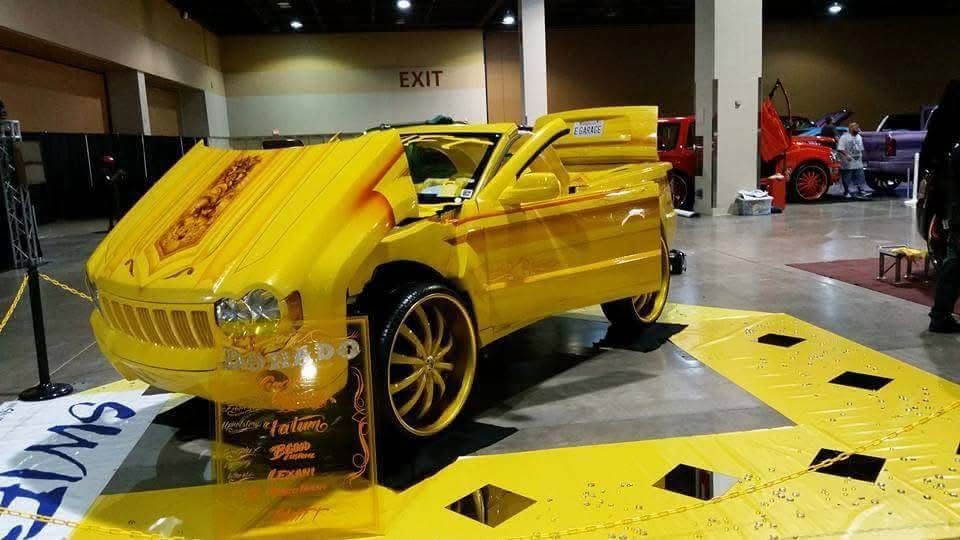 Bright yellow custom lowrider car on display at an indoor auto show.