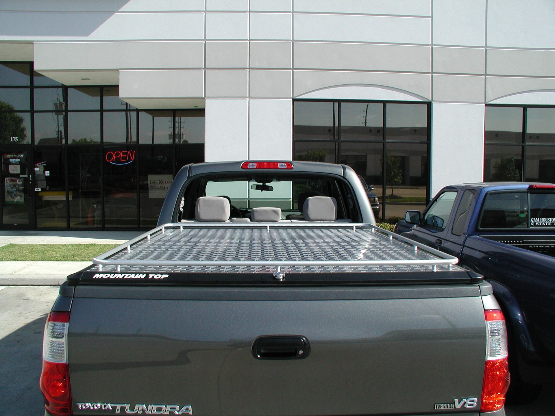 Gray Toyota Tundra with a silver Mountain Top bed cover parked in front of a building.