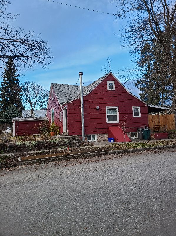 A red house with a chimney on the side of it is sitting on the side of the road