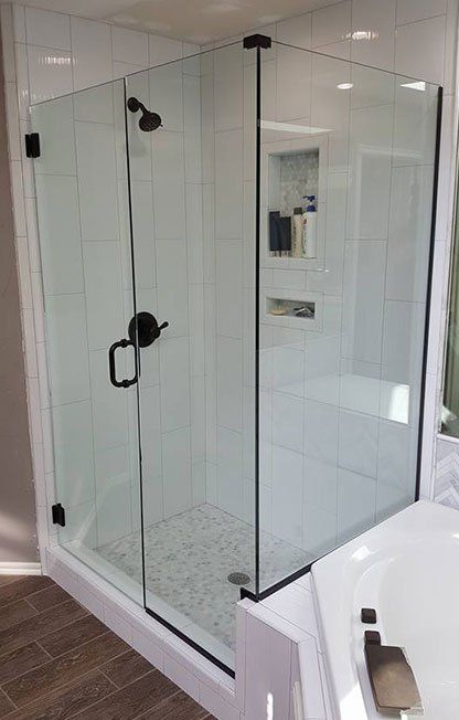 Glass walk-in shower with black fixtures and white tiled walls in a bathroom