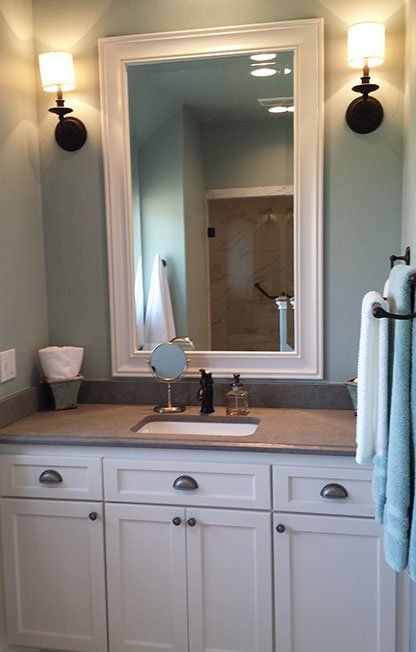 White bathroom vanity with mirror, sink, wall sconces, and towel rack