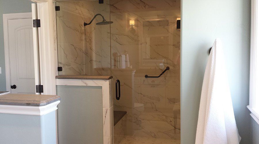 Bathroom with walk-in tiled shower, glass door, and towel hanging by a bright window.
