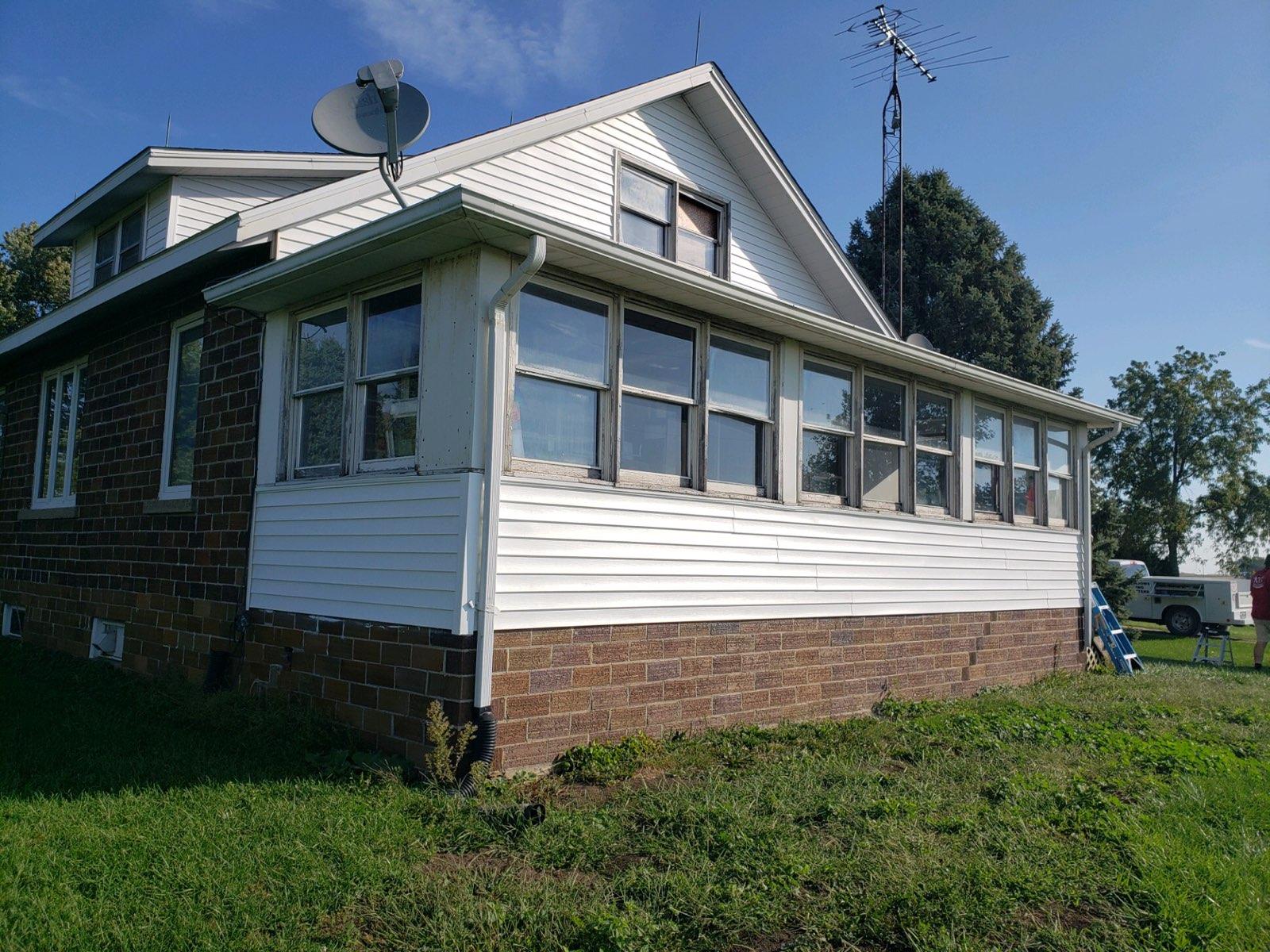 Two-story house with white siding and windows, surrounded by grass under a blue sky.