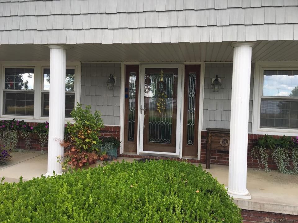 Front entrance with white columns, door, windows, and lush greenery.