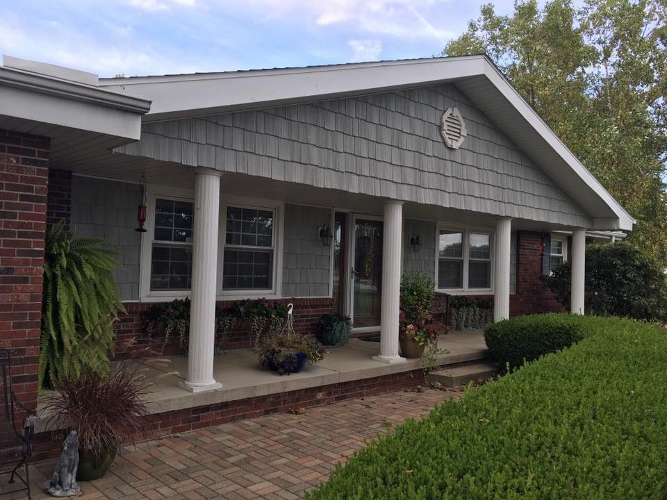 A one-story house with a porch featuring white columns and gray siding, with red brick on the sides.