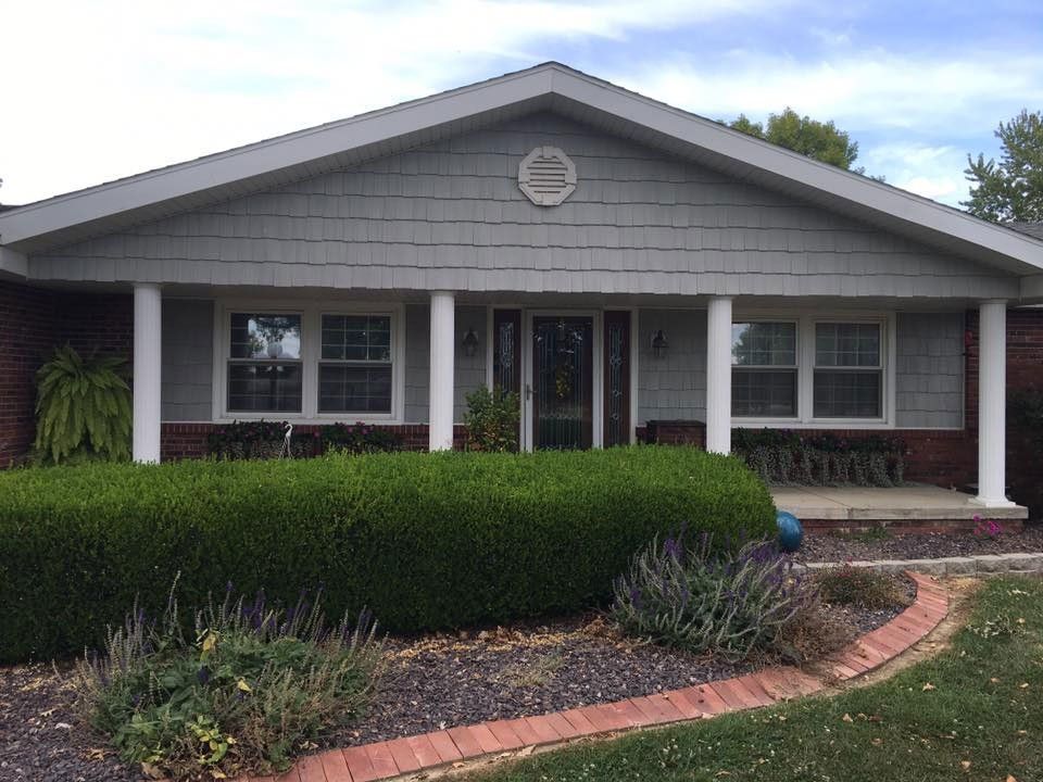 Ranch-style house with gray siding, white columns, brick accents, and well-manicured landscaping.