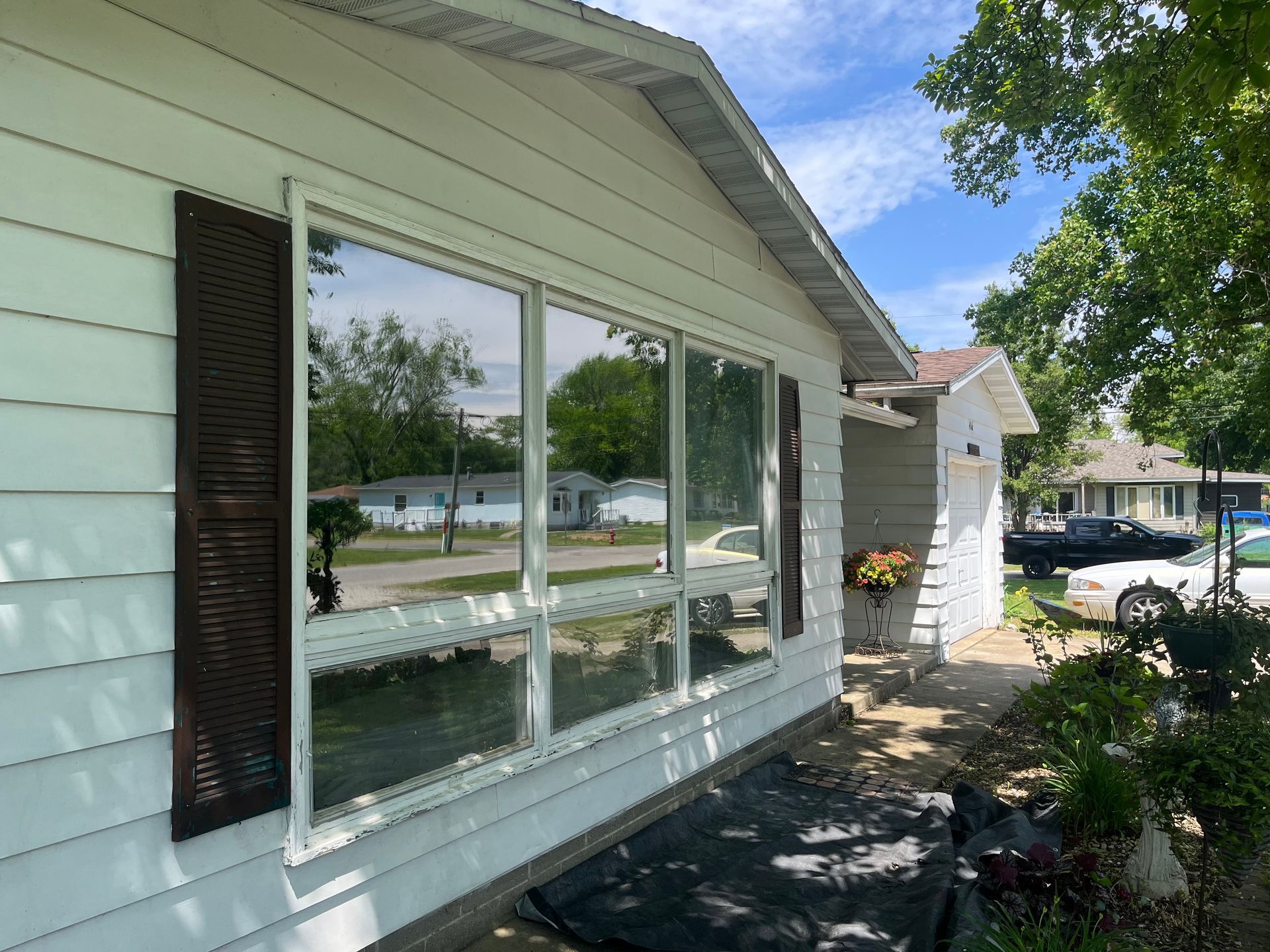 White house with large windows reflecting trees and sky; brown shutters on the left.
