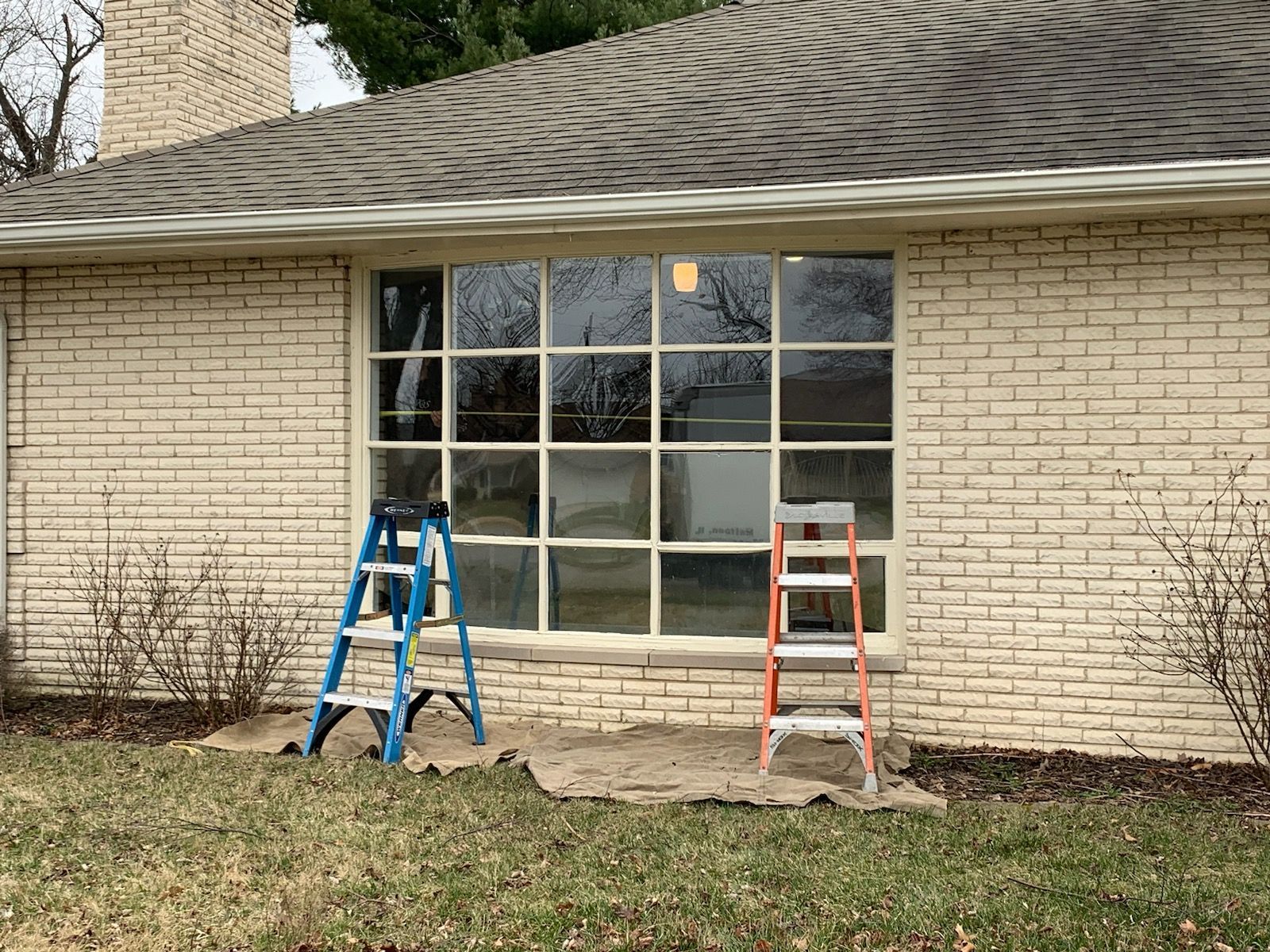 Two ladders in front of a large window on a brick building.