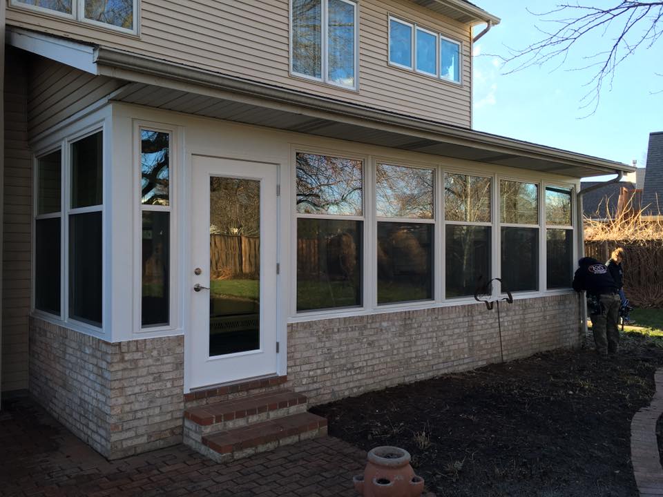 Sunroom addition with white trim, brick facade, and clear windows. Door to backyard.