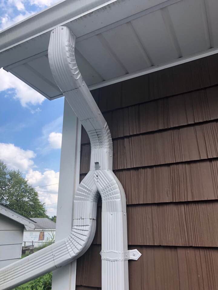 White gutter system attached to a brown-sided building. Gutter extends down the side and splits into two.