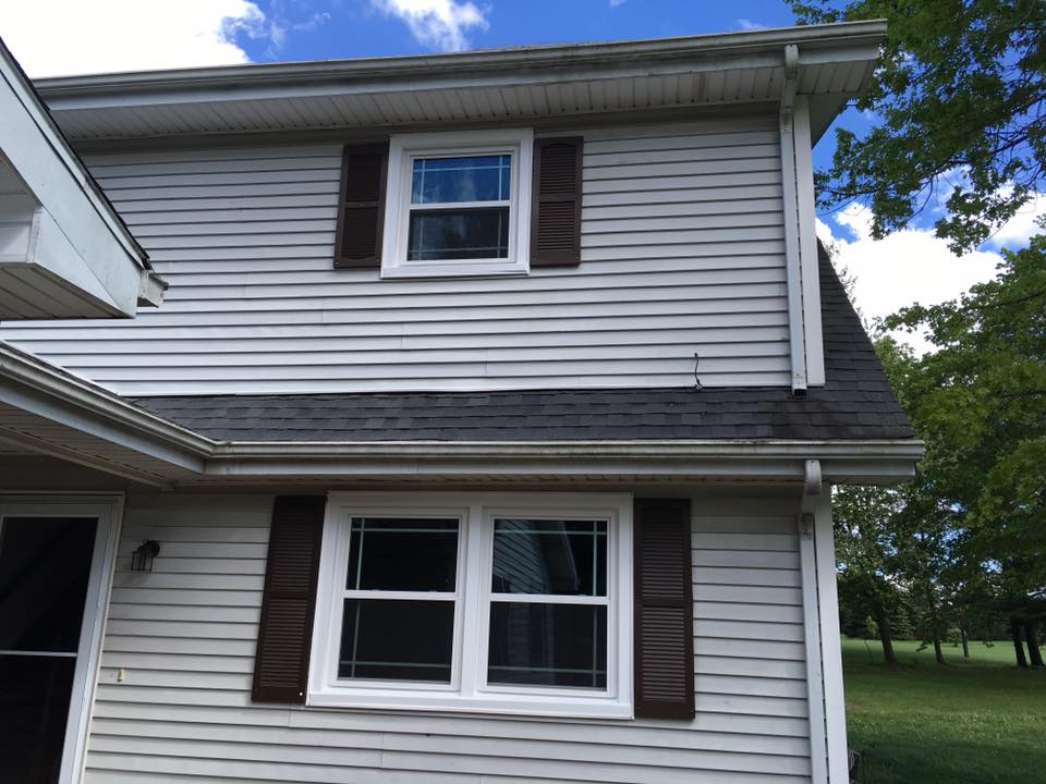 Two-story house with white siding, brown shutters, and windows. Cloudy sky and green grass are in view.