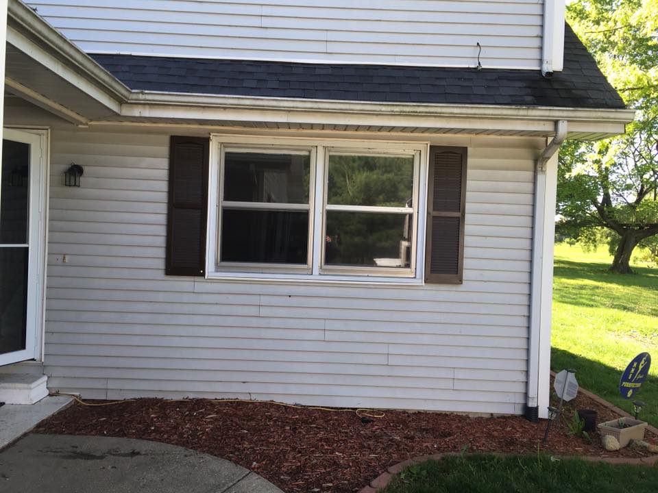Exterior of a light gray house with a window, brown shutters, and dark mulch.