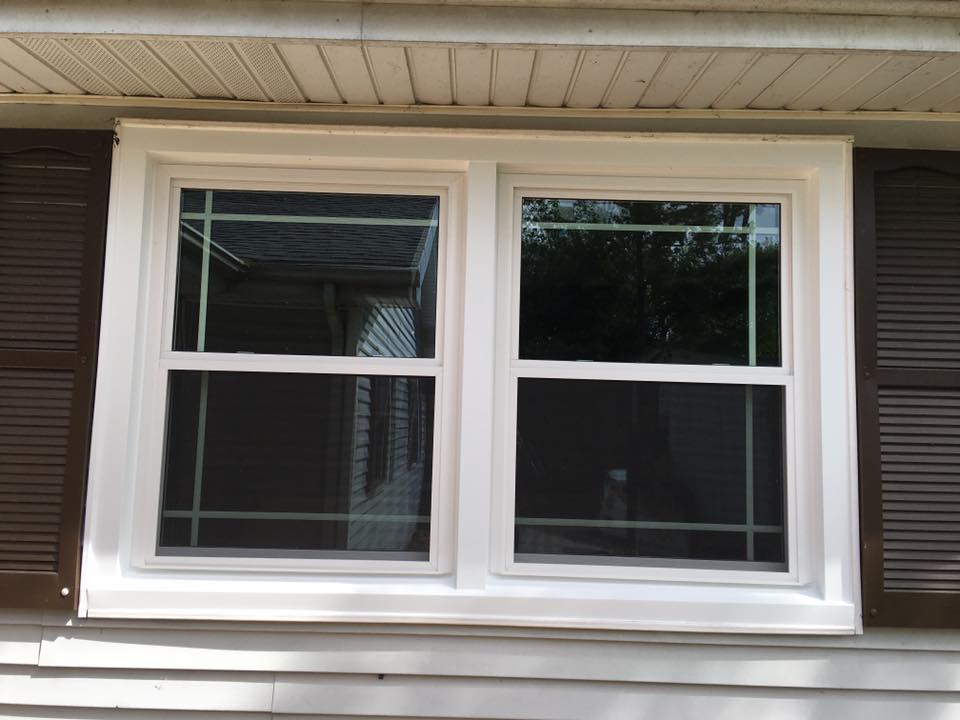 White double-hung window with brown shutters on a house with white siding.