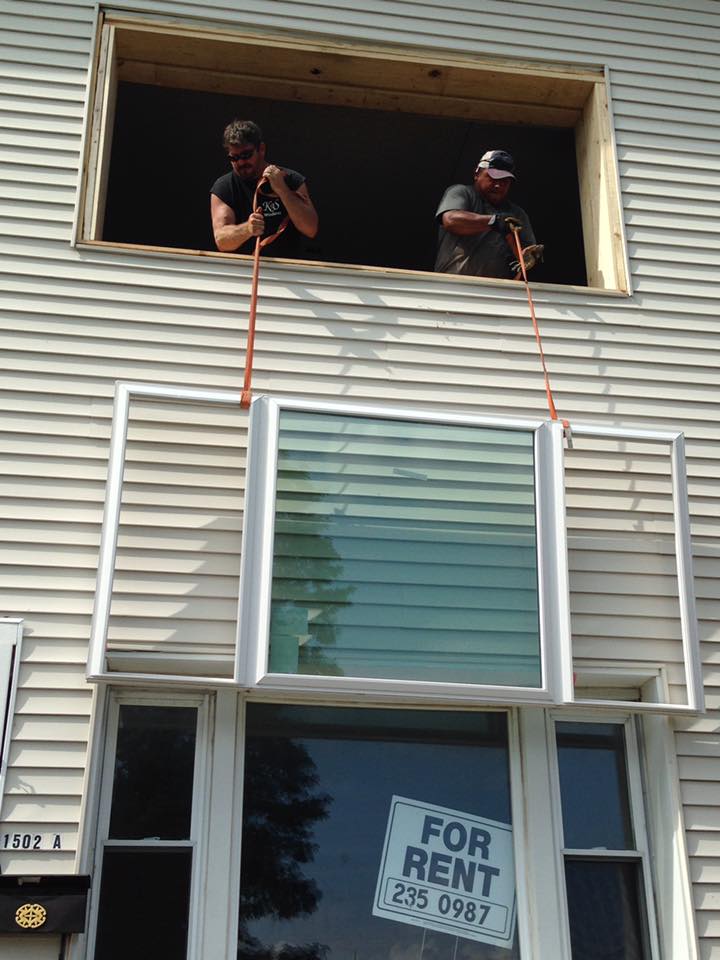 Two men installing a window from an upper-floor opening, with an existing window below, and a 