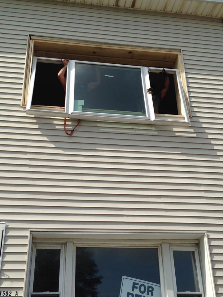 Two people installing a white window in a house opening.