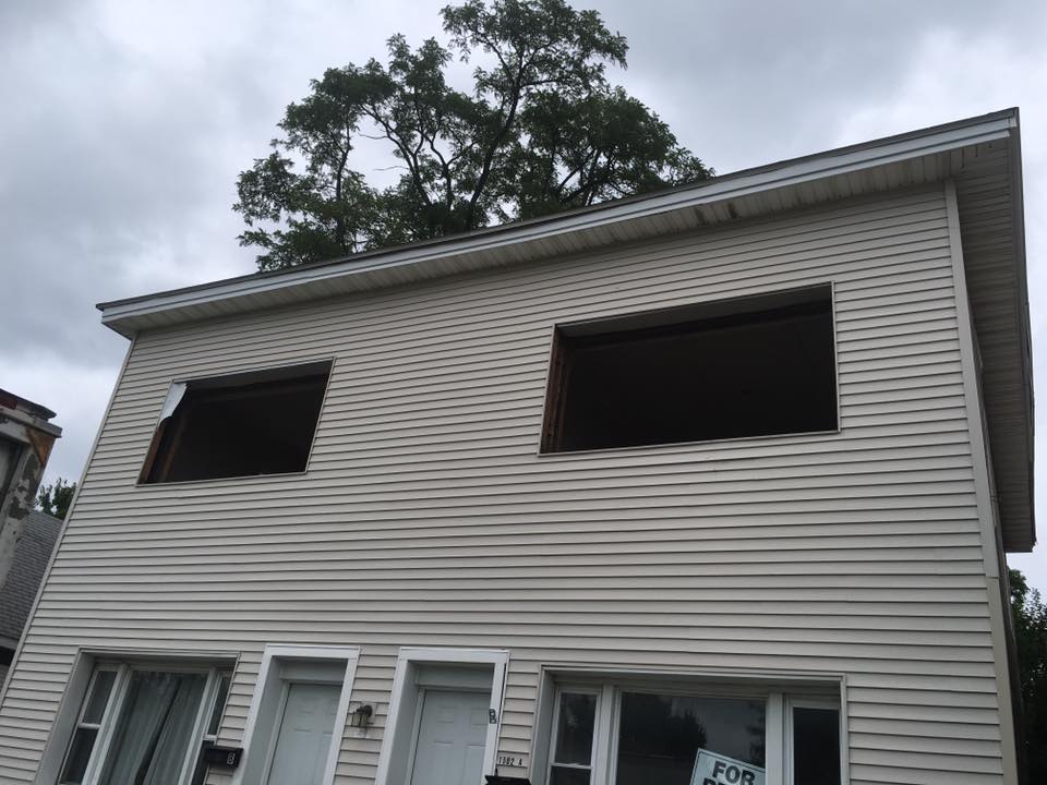 Two-story building with boarded up windows, light siding, overcast sky.