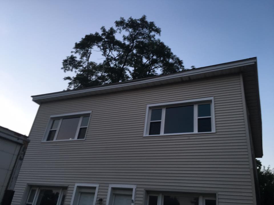Two-story beige house with windows, topped by a tree against a twilight sky.