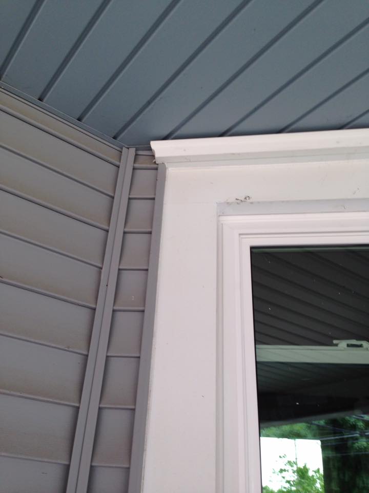 Gray siding and blue soffit meet a white window frame with decorative trim.