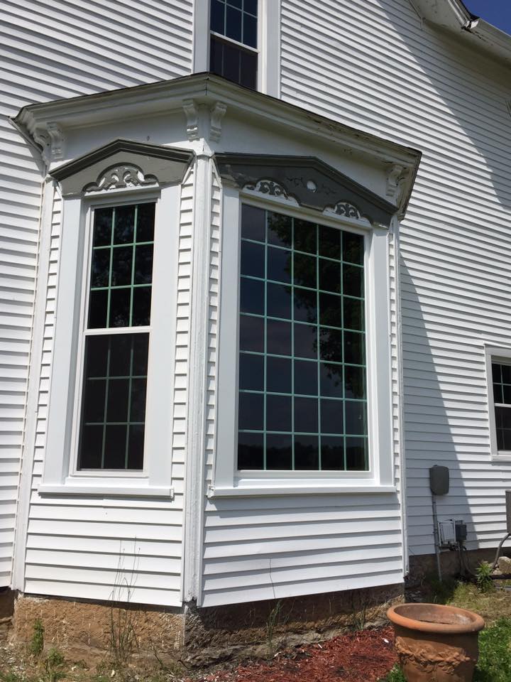 White clapboard house with a bay window, dark glass, decorative trim.