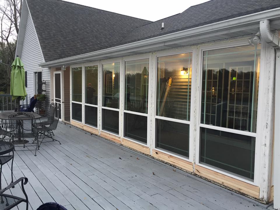 A deck with a sunroom, featuring large windows reflecting light, adjoined to a house.