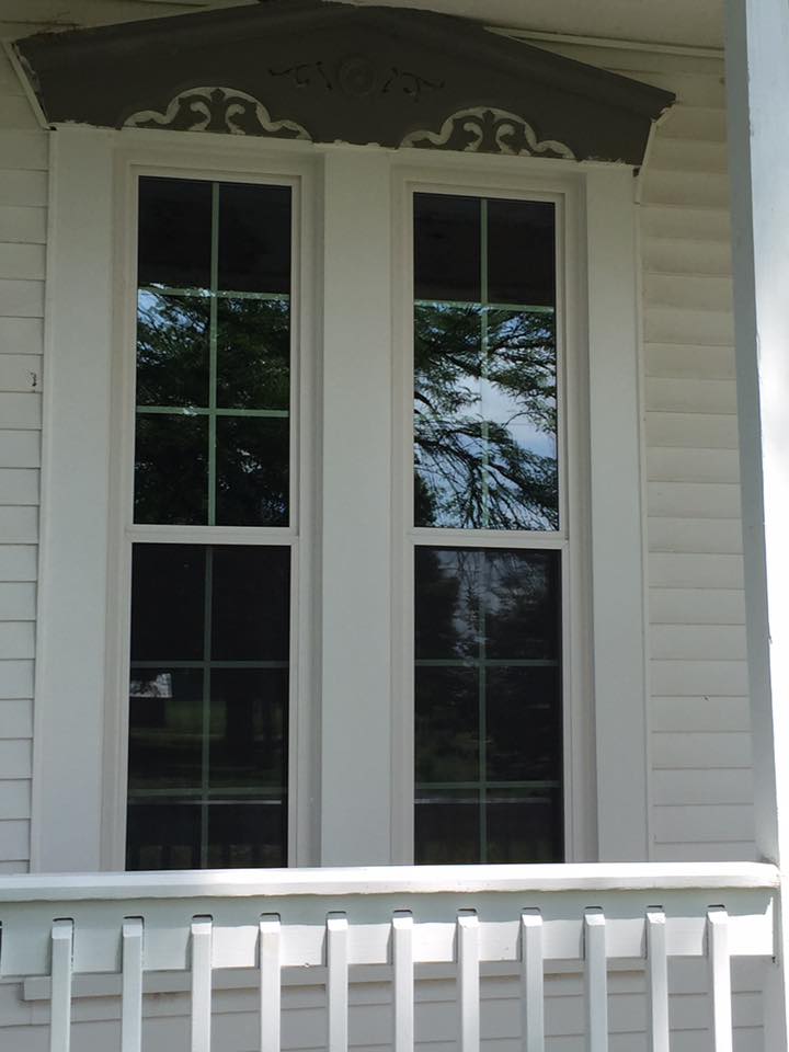 Two tall, white windows on a white house, with dark ornate trim above.