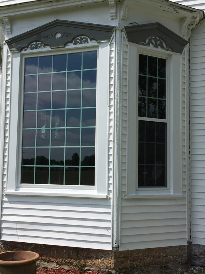 White house with a bay window, gray decorative trim, and a grid-patterned window.