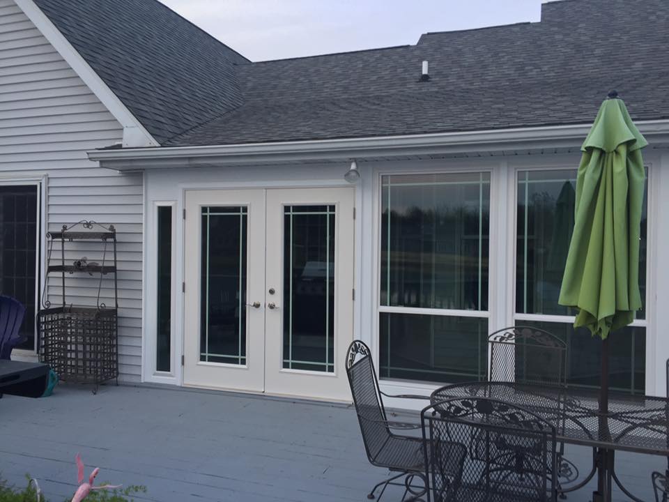 A back deck with French doors and a green umbrella next to a round table and chairs.