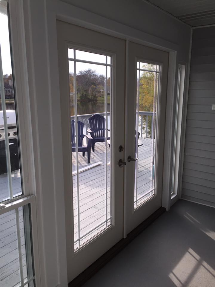 French doors open to a deck with blue chairs, leading to a water view.