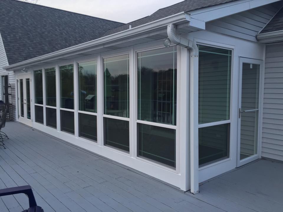 Sunroom addition with white frames and many windows on a gray deck, attached to a gray house.