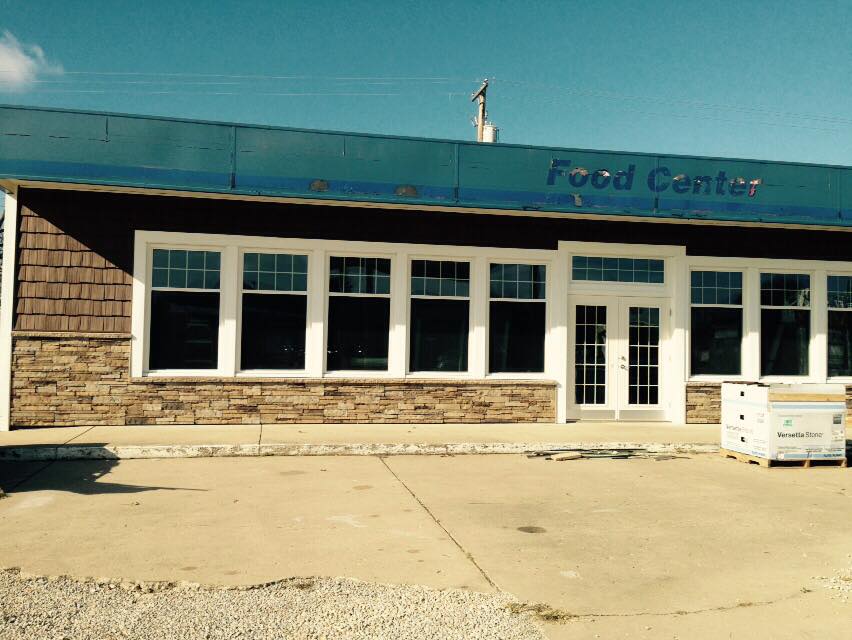 Food Center storefront with brown siding, stone accents, and windows; parked outside on a sunny day.