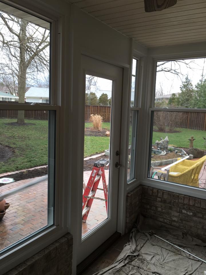 Sunroom interior with door and windows looking out to a backyard with a ladder leaning against the door.