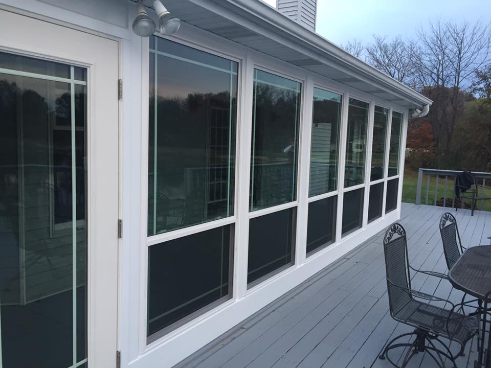 Sunroom with large windows, white frames, and gray deck. Outdoor setting with chairs and table.