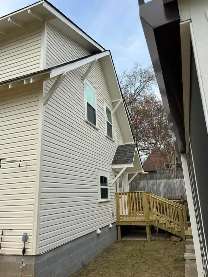 A white house with a wooden deck next to it.