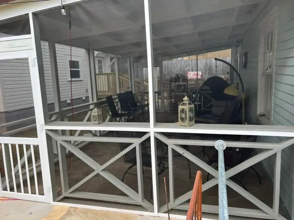 A screened in porch with chairs , tables and lanterns.