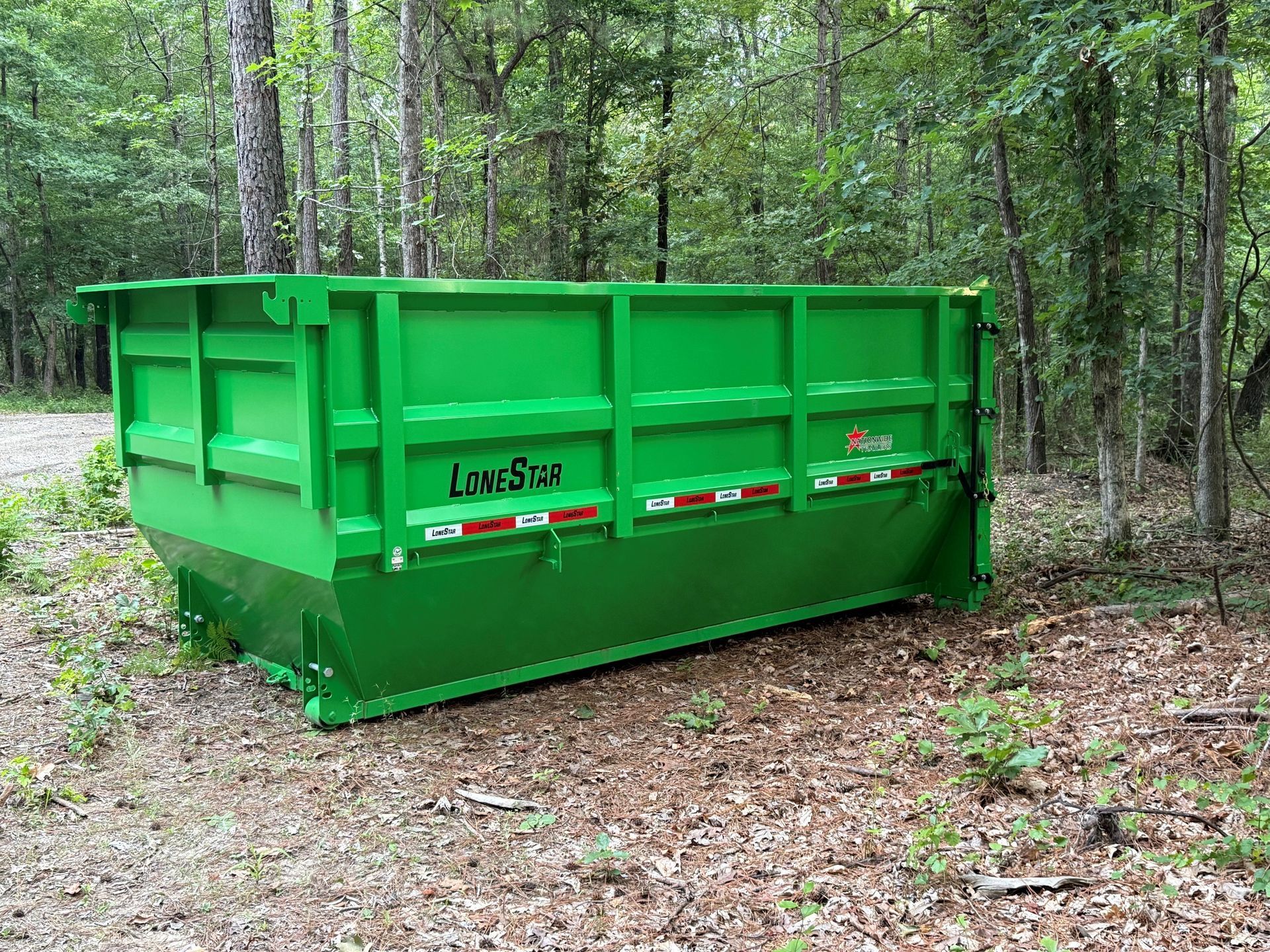Green industrial dumpster in a wooded outdoor area