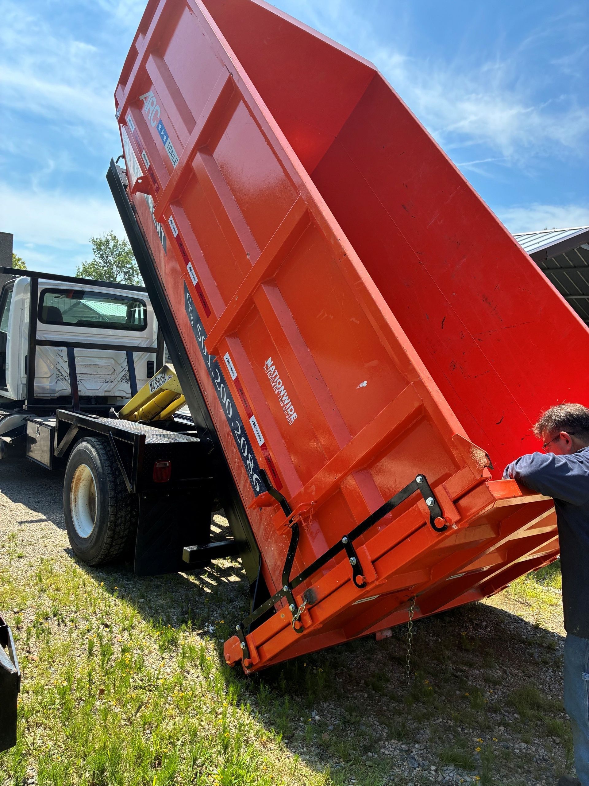 Truck with a raised red dump bed; a person stands beside it outdoors.
