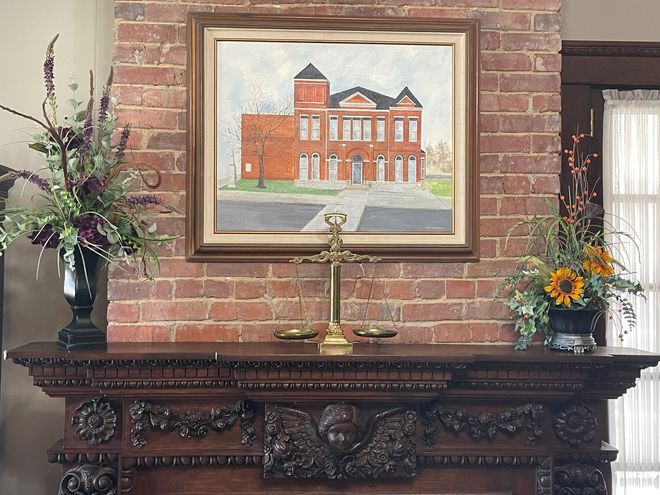 A wooden judge's gavel rests on a block beside a gold scales of justice in a courtroom setting.