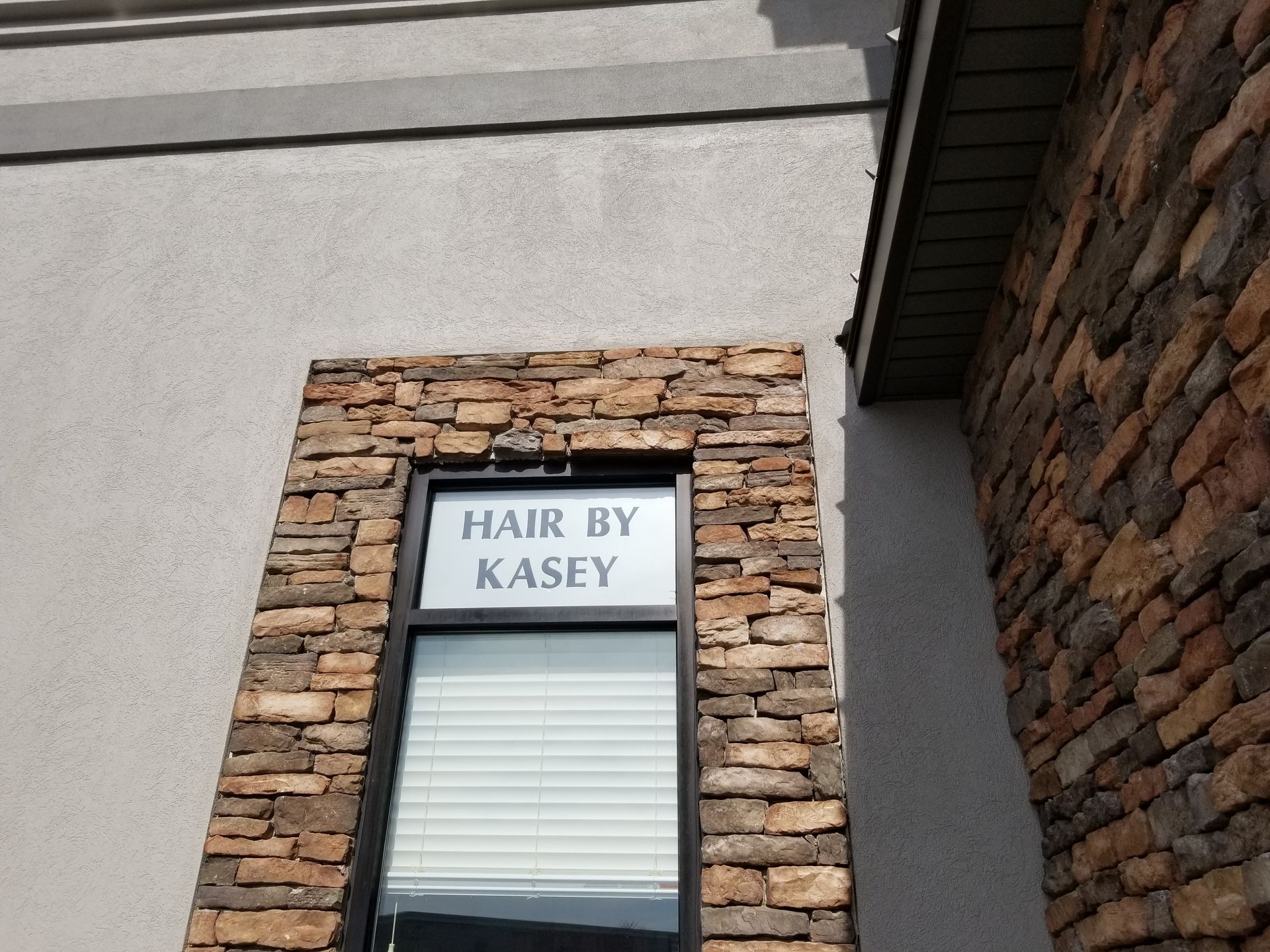 A sign for hair by kasey hangs above a window