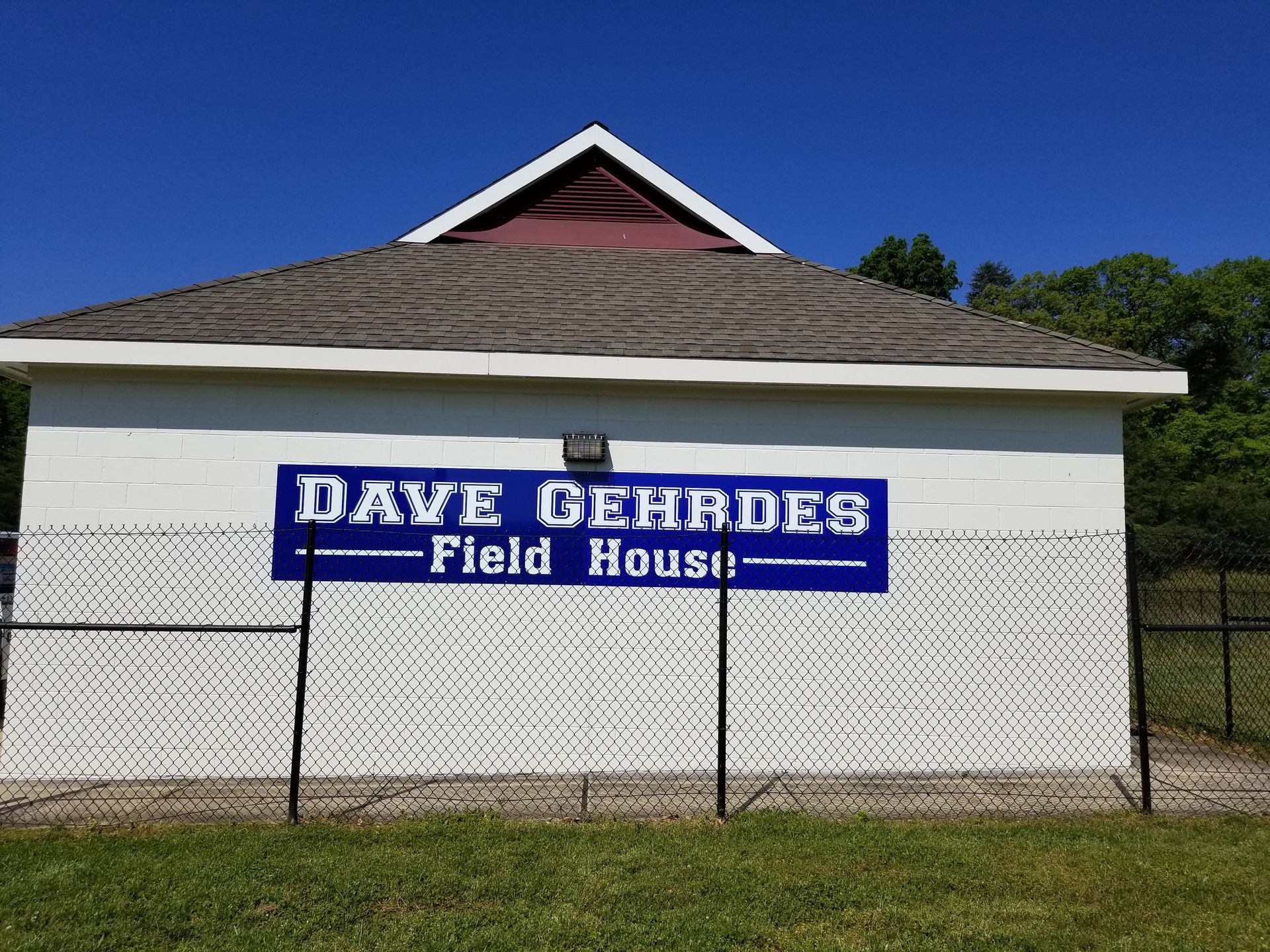 A white building with a blue sign that says dave gehrdes field house