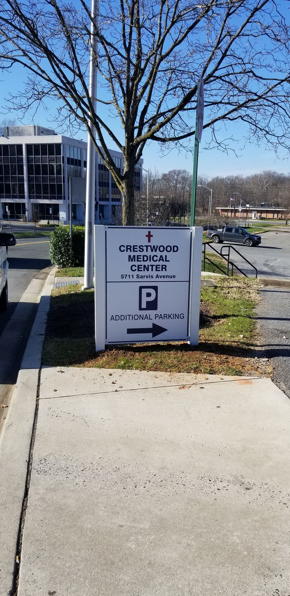A parking sign is sitting on the sidewalk next to a tree.