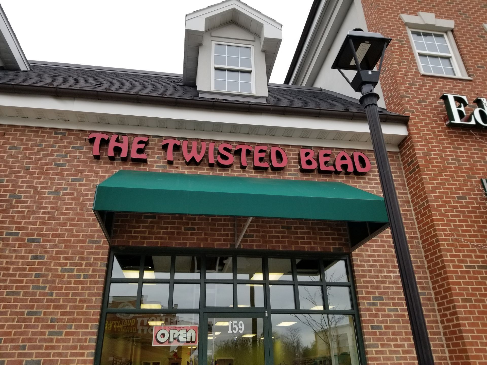 A brick building with a green awning that says the twisted bead