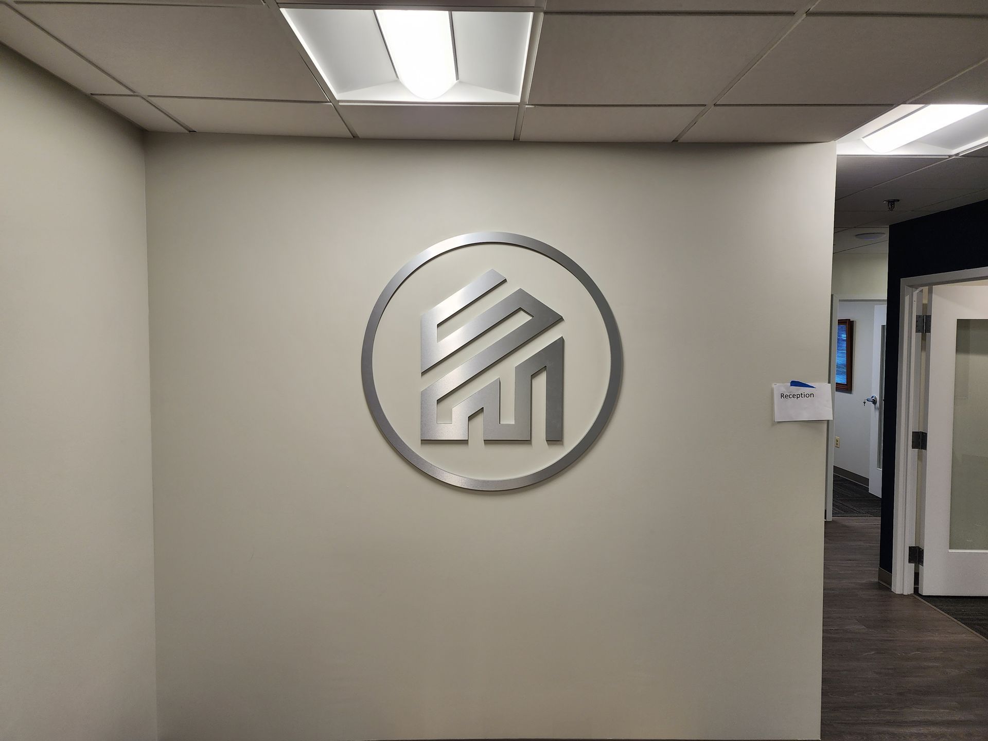 A silver logo on a white wall in a hallway.