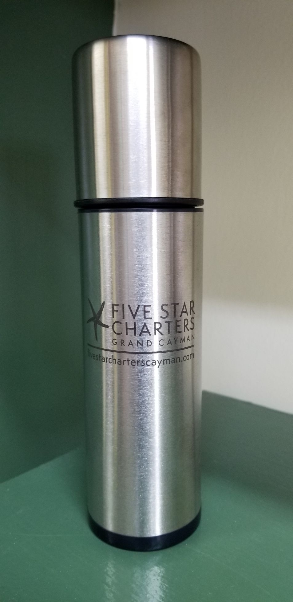 A stainless steel thermos is sitting on top of a green table.