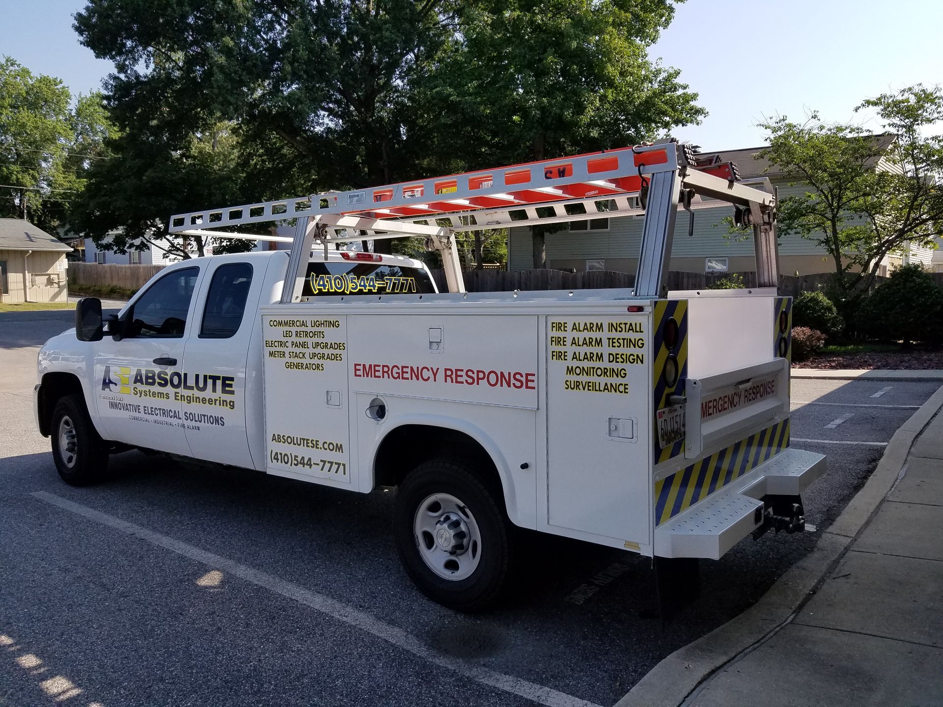 A white utility truck with a ladder on the back is parked in a parking lot.