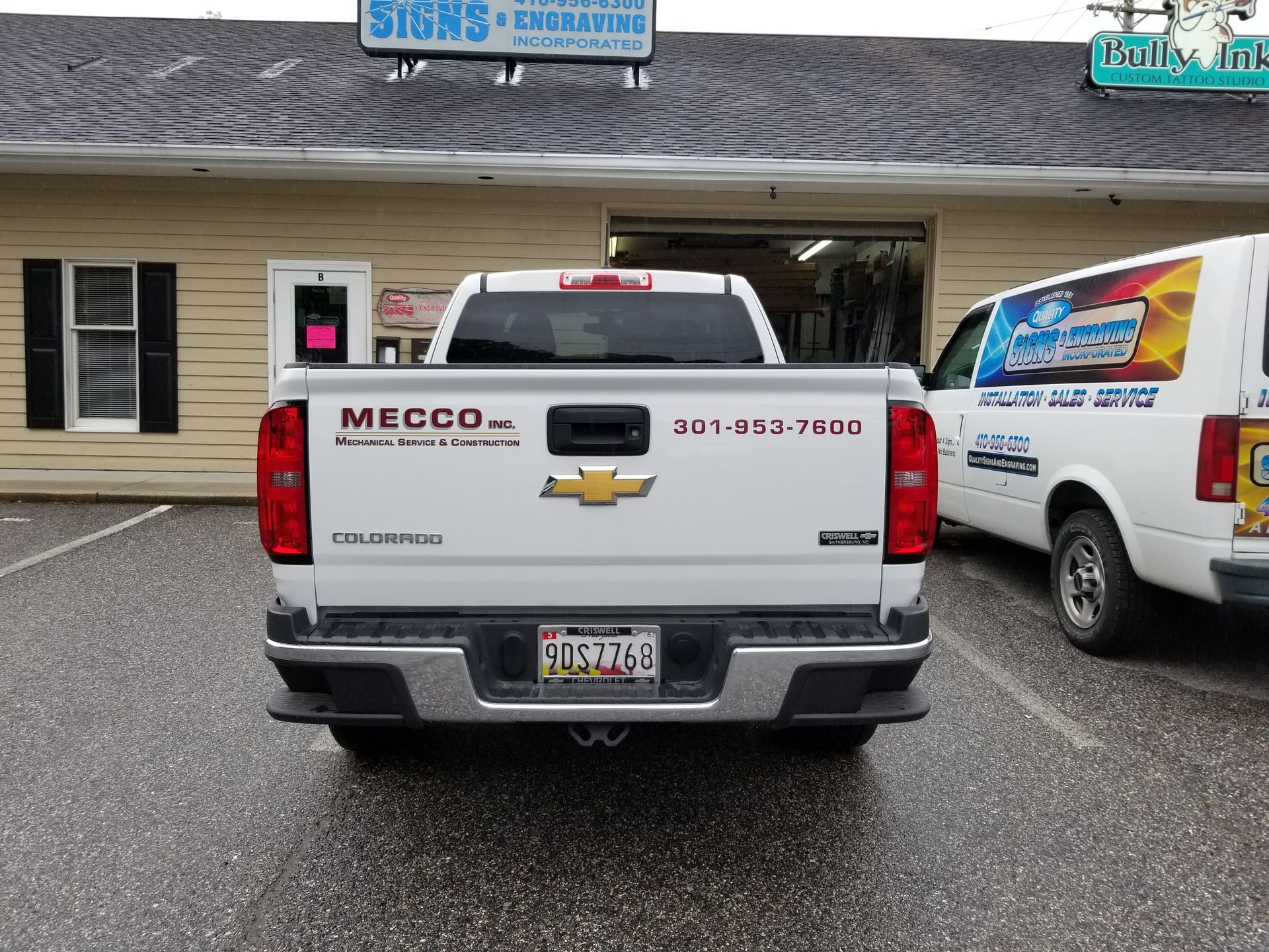 A white truck with the word mecca on the back is parked in front of a building.